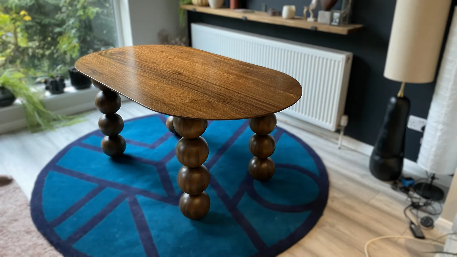 The Orbital dinette table in mahogany on a blue rug by a window